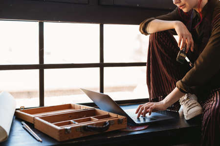 Close up of a young woman artist looking for new ideas on laptop computer sitting on a windowsill in...