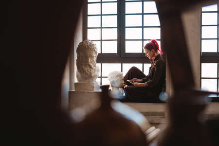 Young white woman painter in an art studio, using laptop computer for ideasの写真素材