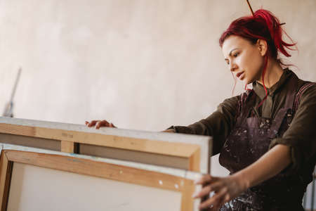 Young white woman painter in an art studio, using laptop computer for ideasの写真素材