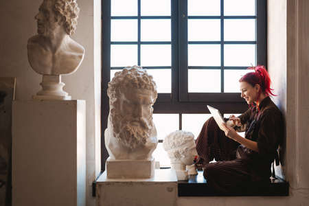 Young white woman painter in an art studio, using laptop computer for ideasの写真素材