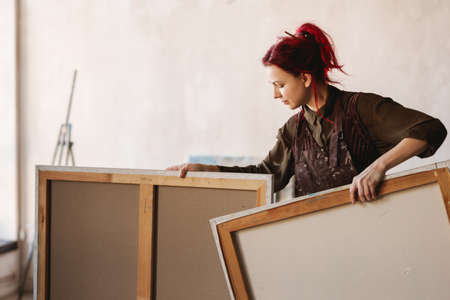 Young white woman painter in an art studio, using laptop computer for ideas