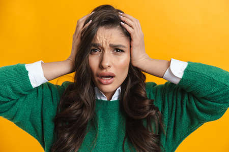 Portrait of a young confused pensive brunette woman standing isolated on a yellow background...