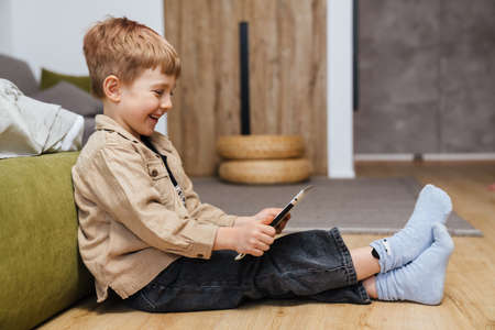 Happy boy toddler holding tablet while sitting in the living room