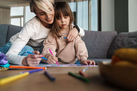 Young mother and her preschooler daughter in the living room, drawing, embracingの写真素材