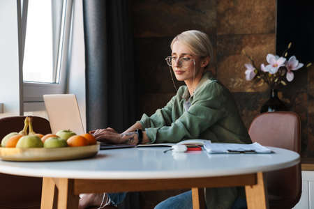 Middle aged blonde woman with short hair studying or working on a video call via laptop computer...