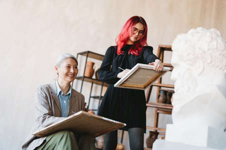 Mature teacher drawing with her student during class in art school indoorsの写真素材