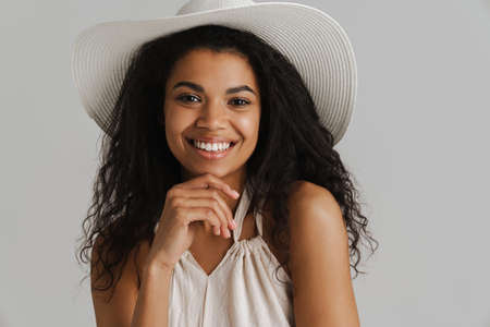 Black young woman in hat smiling and looking at camera isolated over white background