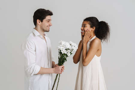 European man giving black woman chrysanthemum bouquet isolated over white backgroundの写真素材