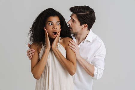 European unshaven man hugging her shocked black girlfriend isolated over white backgroundの写真素材