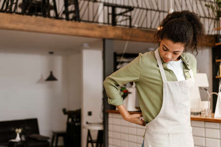 Young black waitress wearing apron while getting ready for work in cafe indoorsの写真素材