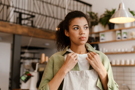 Young black waitress wearing apron while getting ready for work in cafe indoorsの写真素材