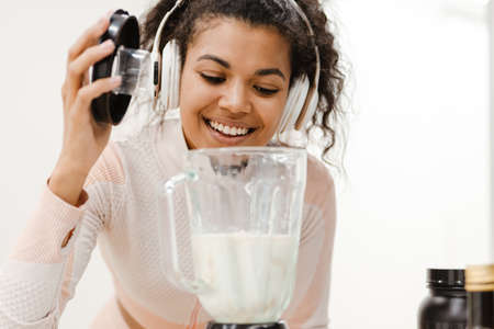 Black woman in headphones smiling and making smoothie at homeの写真素材