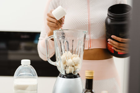 Black woman in headphones making smoothie with protein at homeの写真素材
