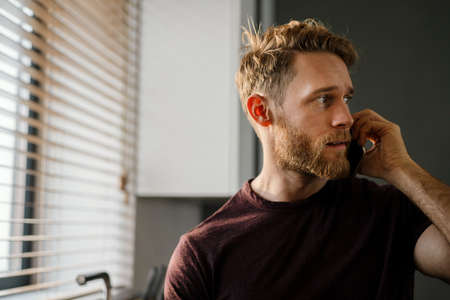 Handsome young man using mobile phone at the kitchen