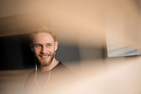 Close up photo of young happy man in earphones in the kitchen at homeの写真素材