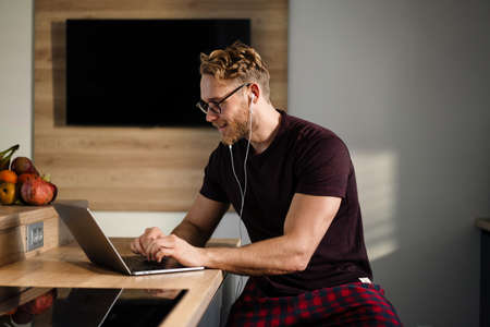 Young attractive man working remotely and heaving a meeting on a laptop while wearing earphonesの写真素材