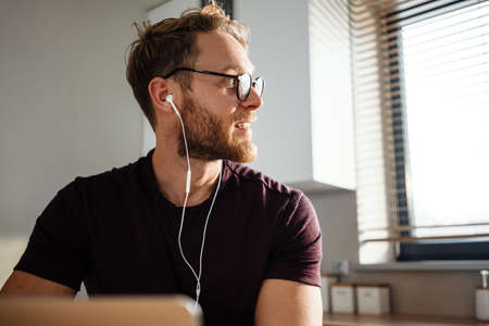 Young attractive man working remotely and heaving a meeting on a laptop while wearing earphonesの写真素材