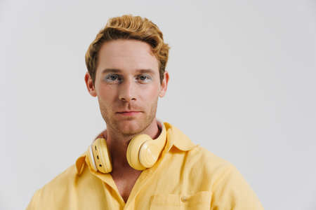 Ginger young man with headphones posing and looking at camera isolated over white wallの写真素材