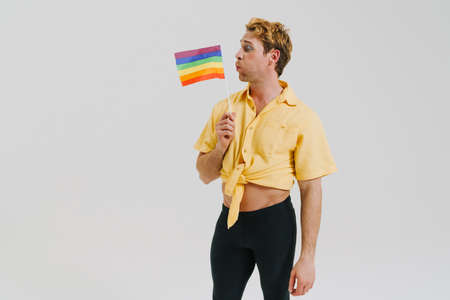 Ginger young man holding and blowing at rainbow flag isolated over white wallの写真素材