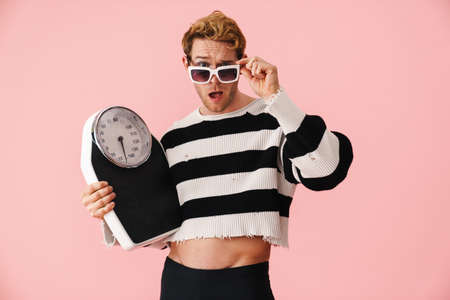 Ginger young shocked man wearing sunglasses posing with scales isolated over pink wallの写真素材