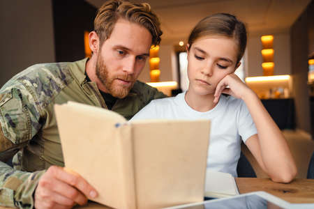 Masculine focused military man doing homework with her daughter at homeの写真素材