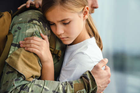 Masculine sad military man hugging her upset daughter indoorsの写真素材