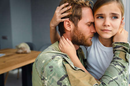 Masculine sad military man hugging her upset daughter indoorsの写真素材