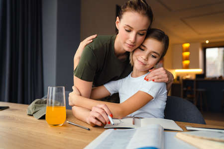 Beautiful focused military woman hugging while doing homework with her daughter at homeの写真素材