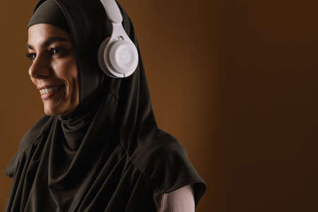 Young muslim woman in hijab listening music with headphones isolated over brown backgroundの写真素材
