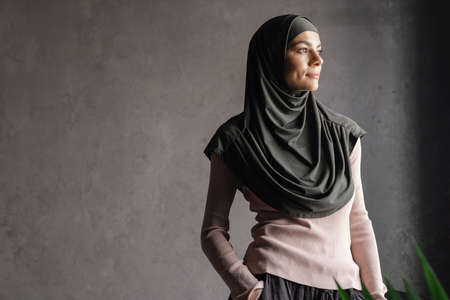 Young muslim woman in hijab posing and looking aside isolated over grey background