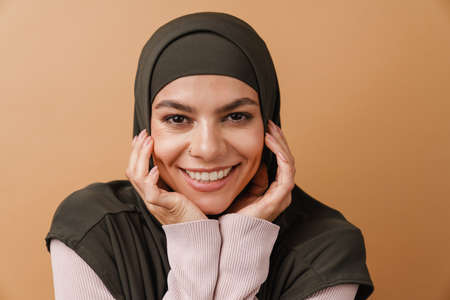 Young muslim woman in hijab smiling and looking at camera isolated over beige background