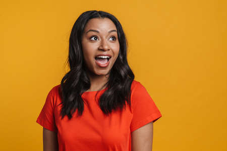 Young black excited woman smiling and looking aside isolated over yellow background