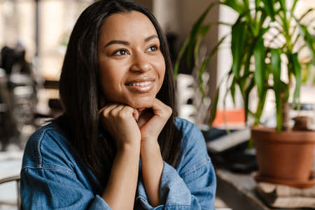 Black young woman smiling and looking aside while sitting in cafeの写真素材