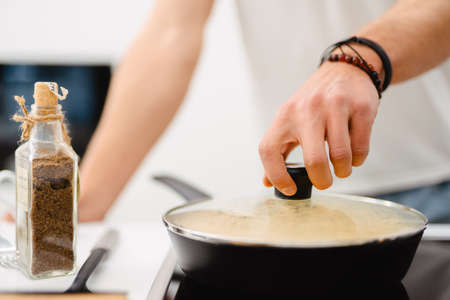 Young white man using frying pan while cooking in kitchen at homeの写真素材