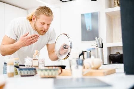 Young white man smelling while cooking in kitchen at homeの写真素材