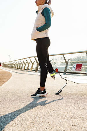 Young sportswoman with prosthesis walking on city bridge