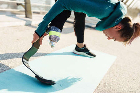 Young sportswoman with prosthesis doing exercise while working out on city bridge