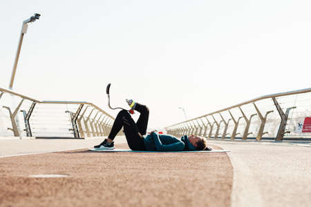 Young sportswoman with prosthesis doing exercise while working out on city bridgeの写真素材