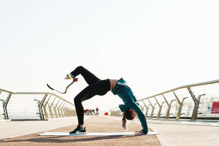 Young sportswoman with prosthesis doing exercise while working out on city bridge