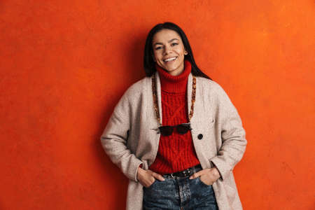 Young hispanic woman laughing and looking at camera isolated over orange wall