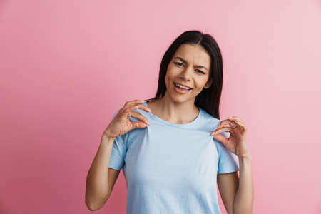 Young hispanic woman smiling and holding her t-shirt isolated over pink wall