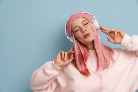Young woman singing while listening music with headphones isolated over blue wallの写真素材