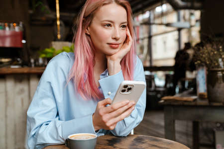 Young white woman with pink hair using mobile phone while sitting in cafeの写真素材