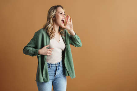 Excited beautiful woman looking and screaming aside isolated over beige wall
