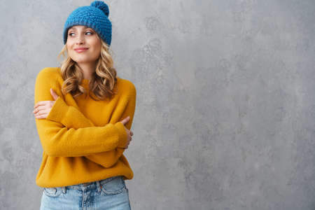 Portrait of a happy young girl dressed in winter clothes standing isolated over gray background,...