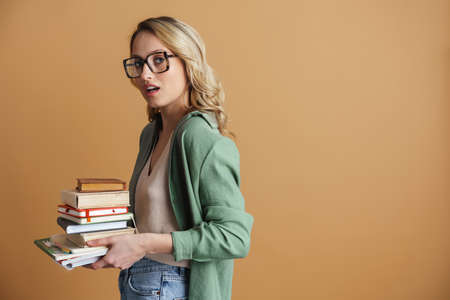 Pretty overloaded girl wearing glasses standing with books isolated over gray backgroundの写真素材