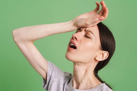 Young brunette woman frowning while gesturing at camera isolated over green backgroundの写真素材