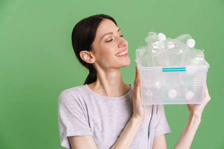 Young brunette woman smiling while posing with plastic waste isolated over green background