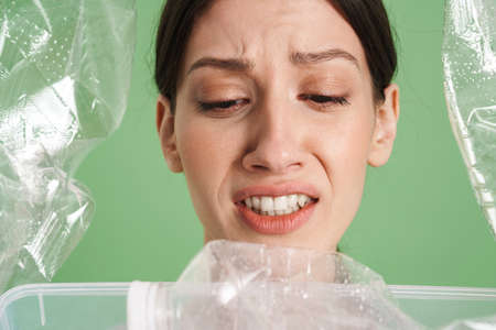 Young confused frowning woman carrying a plastic container full with empty recyclable plastic. Recycling concept close upの写真素材
