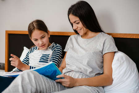 Happy mother and daughter doing homework while laying on bed indoors